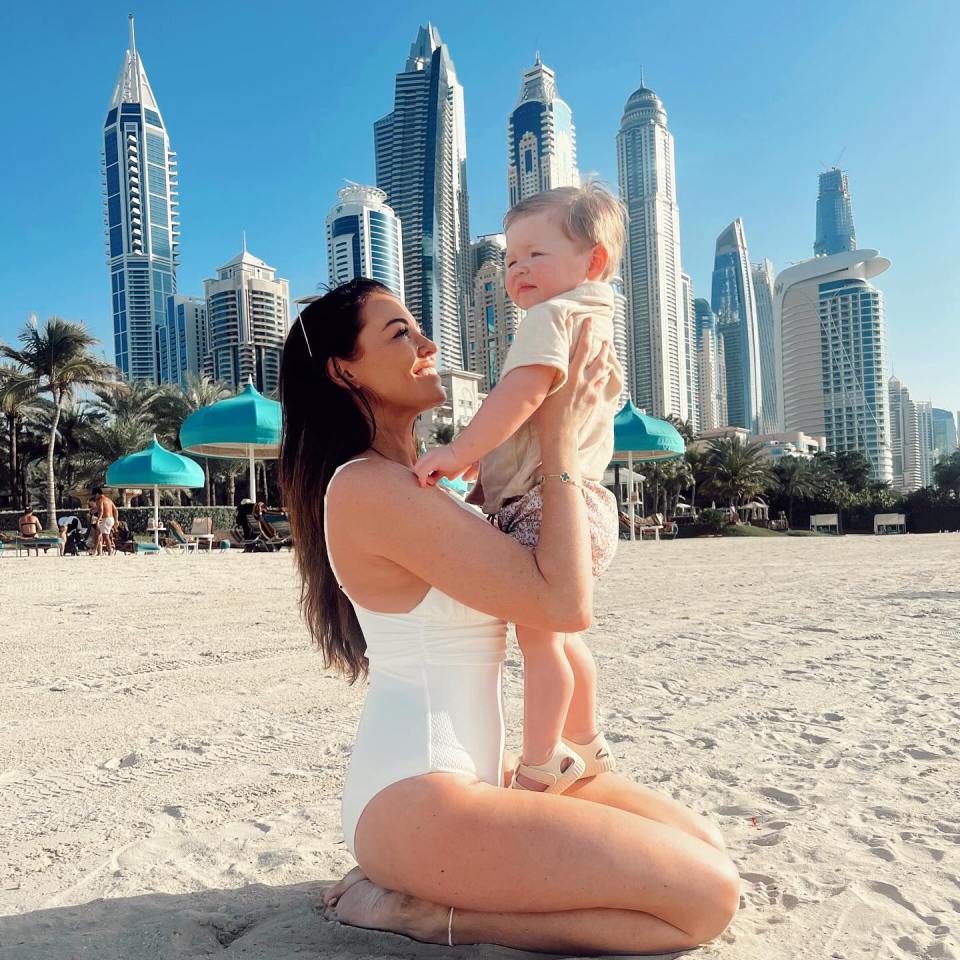 a woman in a white bathing suit holds a baby on the beach