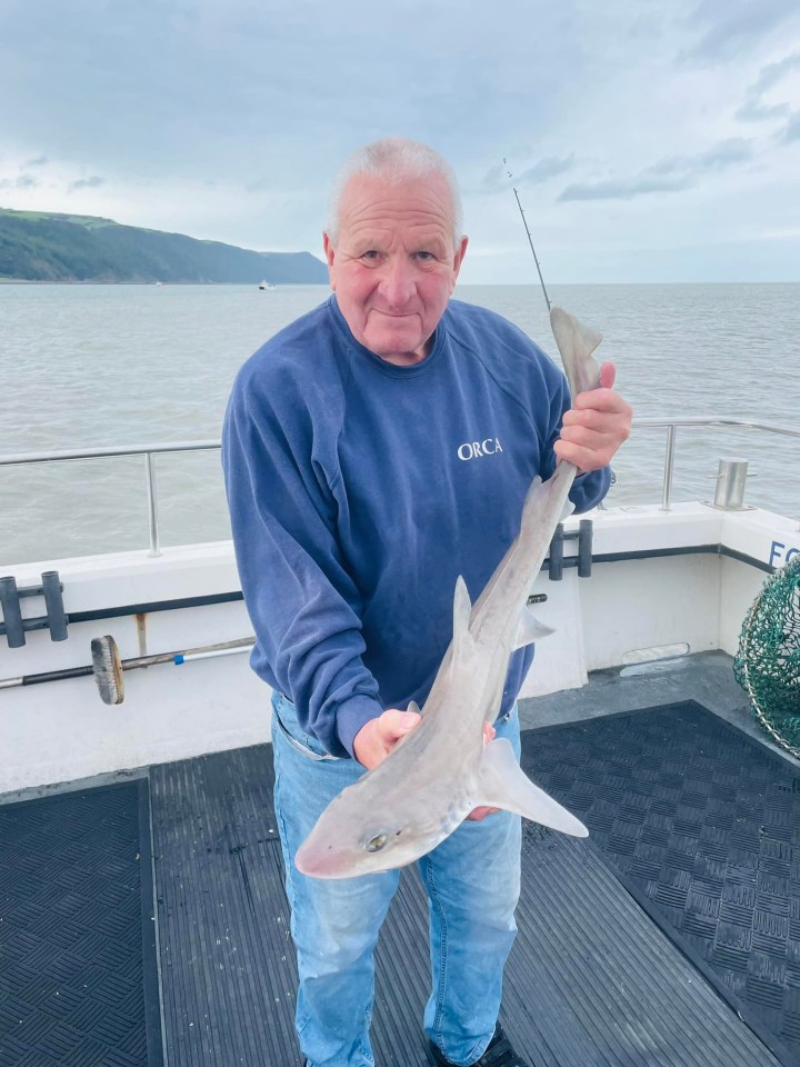 a man on a boat is holding a fish and his shirt says orca