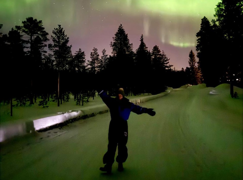 a person with their arms outstretched in front of the aurora borealis