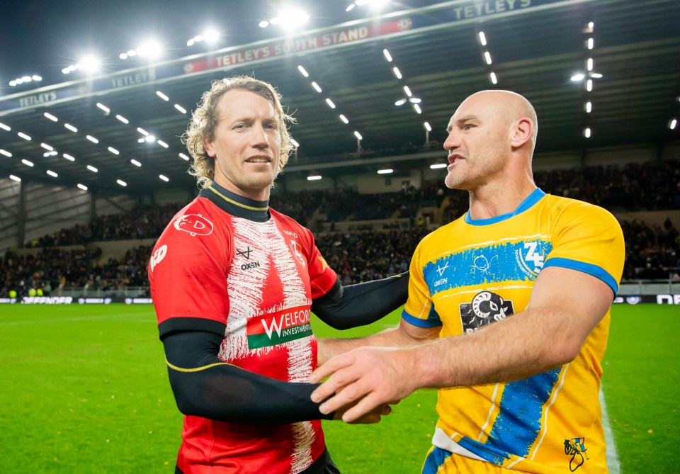 two men shake hands on a soccer field with a sign that says tetley 's team stand in the background