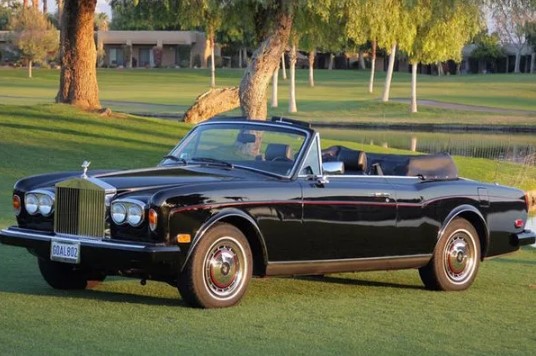 a black rolls royce convertible is parked on a golf course next to a lake .
