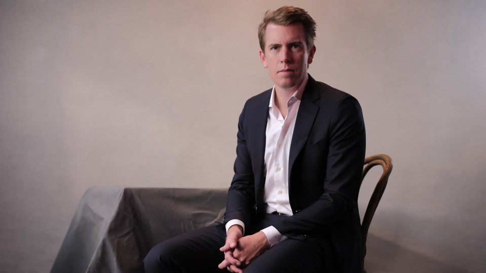 a man in a suit sits in a chair with his hands folded
