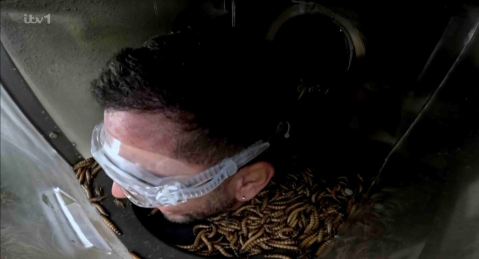 a man wearing safety goggles is surrounded by worms on a tv screen that says itv 1