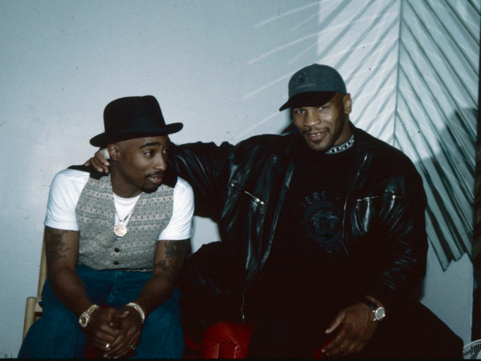 two men sitting next to each other one wearing a guess shirt