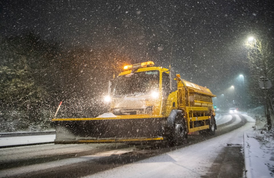 a snow plow drives down a snowy road at night