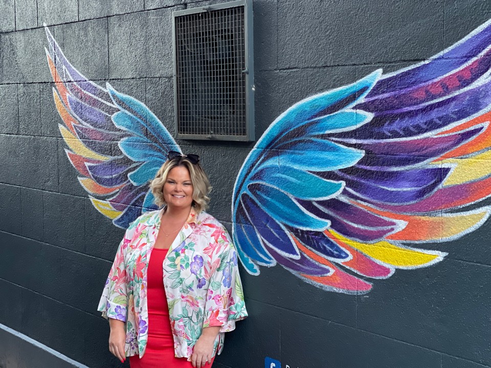 a woman stands in front of a wall with wings painted on it