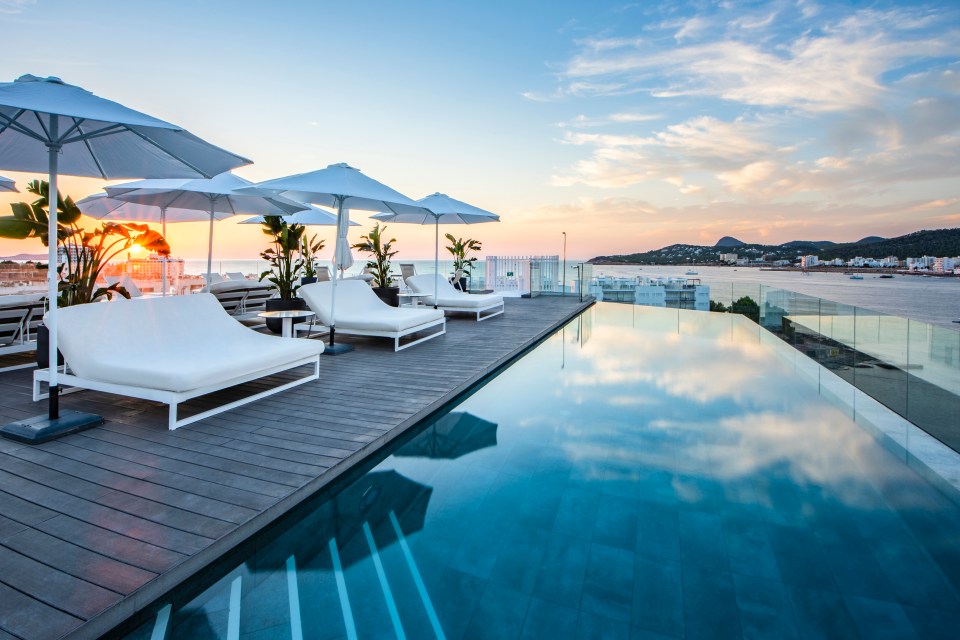 a swimming pool with chairs and umbrellas on the deck