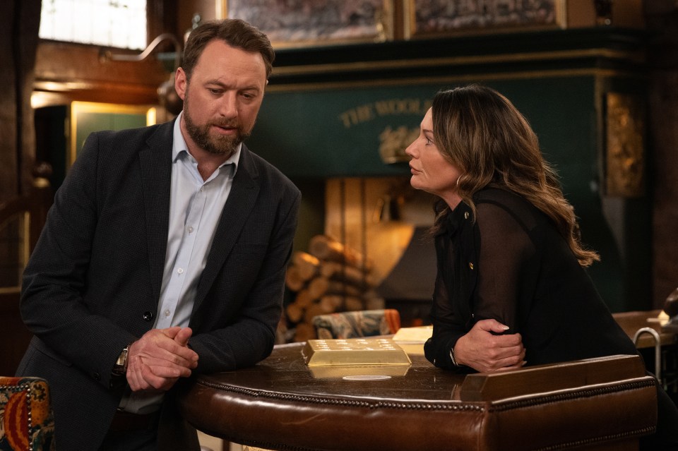 a man and a woman sit at a table in front of a fireplace that says the rock