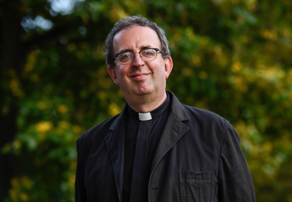 a man wearing glasses and a clergy collar smiles for the camera