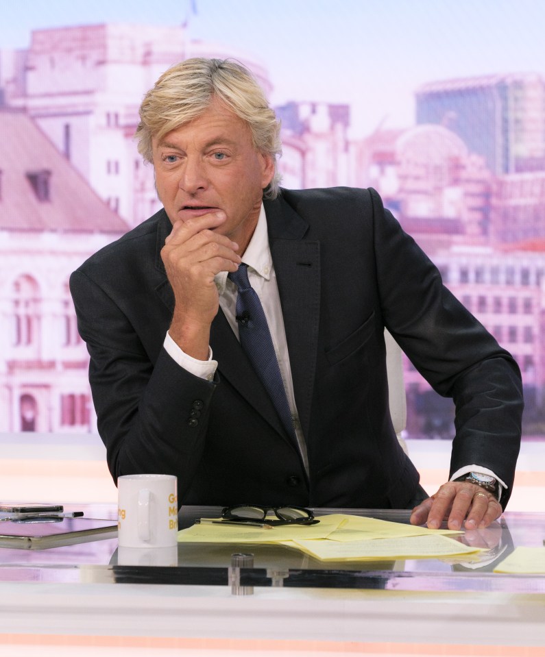 a man in a suit sits at a desk with a cup that says bbc on it