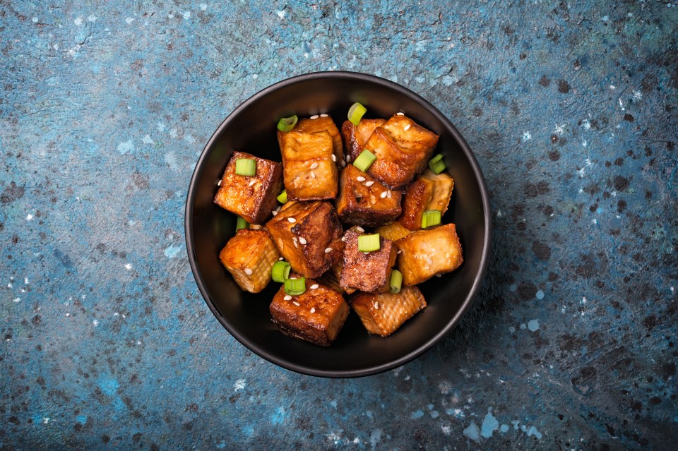 a black bowl filled with fried meat and green onions