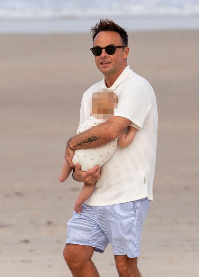 a man wearing sunglasses holds a baby on the beach