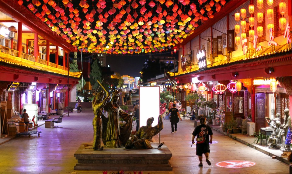 a man wearing a black shirt with chinese writing on it walks down a street