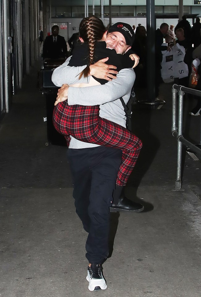 A man carrying a woman in a hug at an airport.