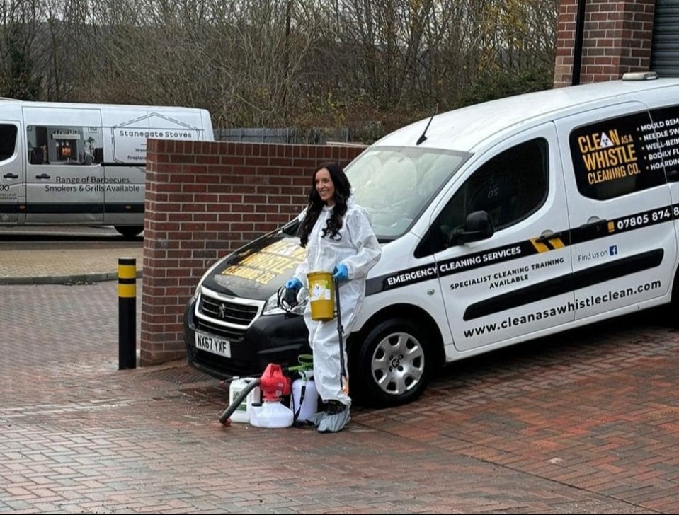 A woman in a hazmat suit stands beside a cleaning company van.