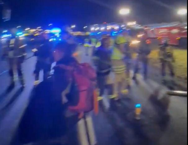 Nighttime scene of emergency responders and bystanders at what appears to be an incident.
