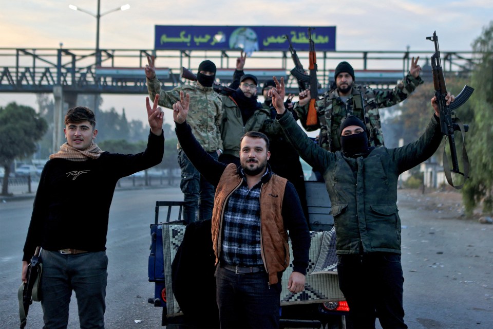 Syrian rebel fighters celebrate at the entrance of Homs province early on December 8, 2024, after rebel forces entered Syria's third city overnight. Hayat Tahrir al-Sham (HTS) and allied anti-goovernment factions have pressed a lightning offensive since November 27, sweeping swathes of the country from government control, including major cities Aleppo, Hama and Homs. (Photo by Aaref WATAD / AFP) (Photo by AAREF WATAD/AFP via Getty Images)
