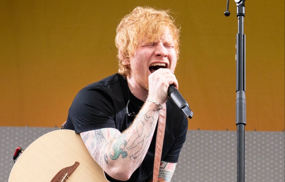 Ed Sheeran performing on stage with an acoustic guitar.