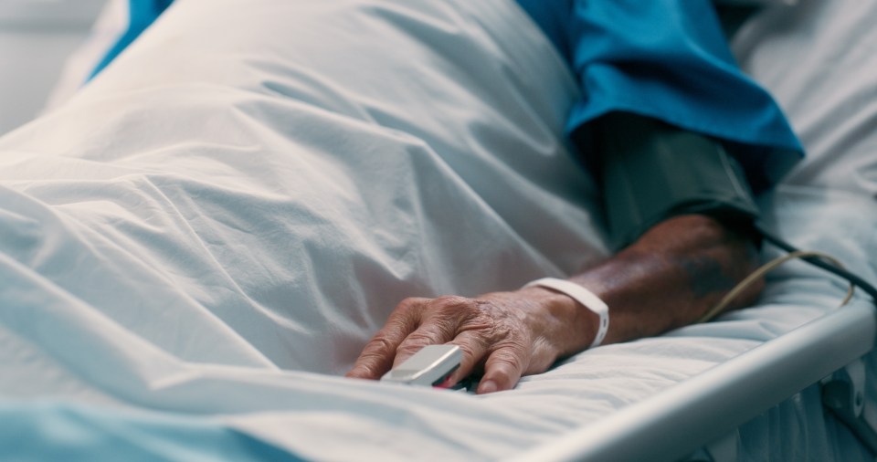 Elderly man's hand resting on a hospital bed.