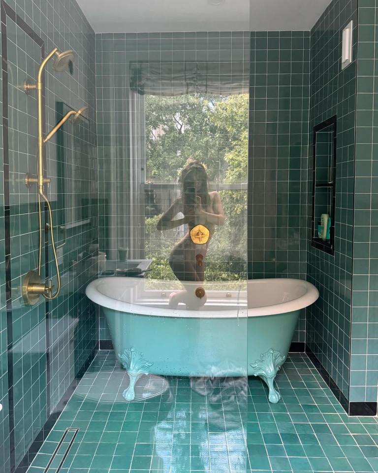A teal clawfoot bathtub in a green-tiled bathroom.