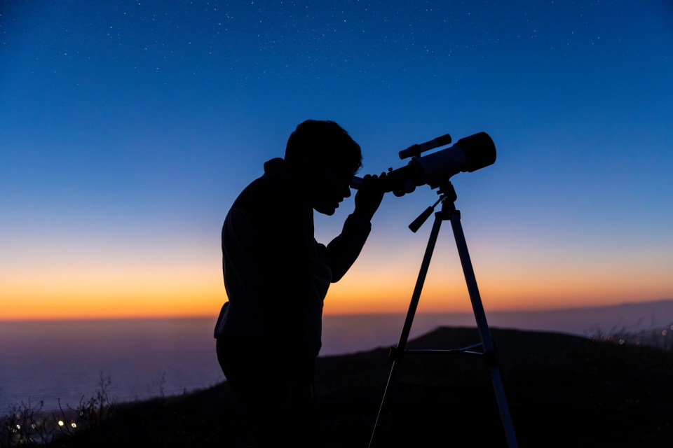 Silhouette of a boy using a telescope at sunset.