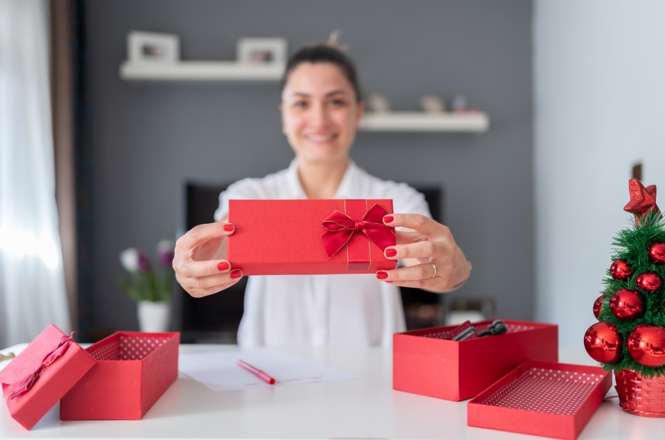 Woman holding out a red Christmas gift box.