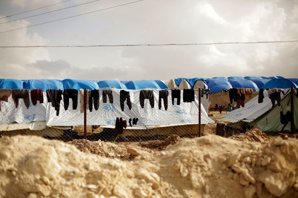 Laundry hanging on a fence in front of tents at a refugee camp.