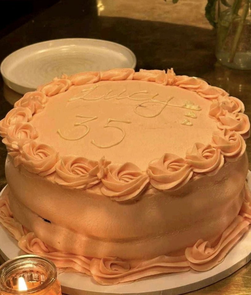 Peach-colored cake decorated with frosting roses and "Lucy 35" written on top.