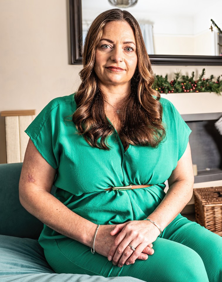 Woman in green dress sits on a teal couch in front of a decorated Christmas tree.