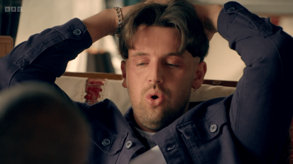 Man with hands behind his head, mouth open.