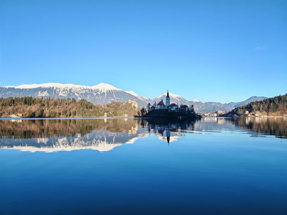 Lake Bled with church and snow-capped mountains reflected in the water.