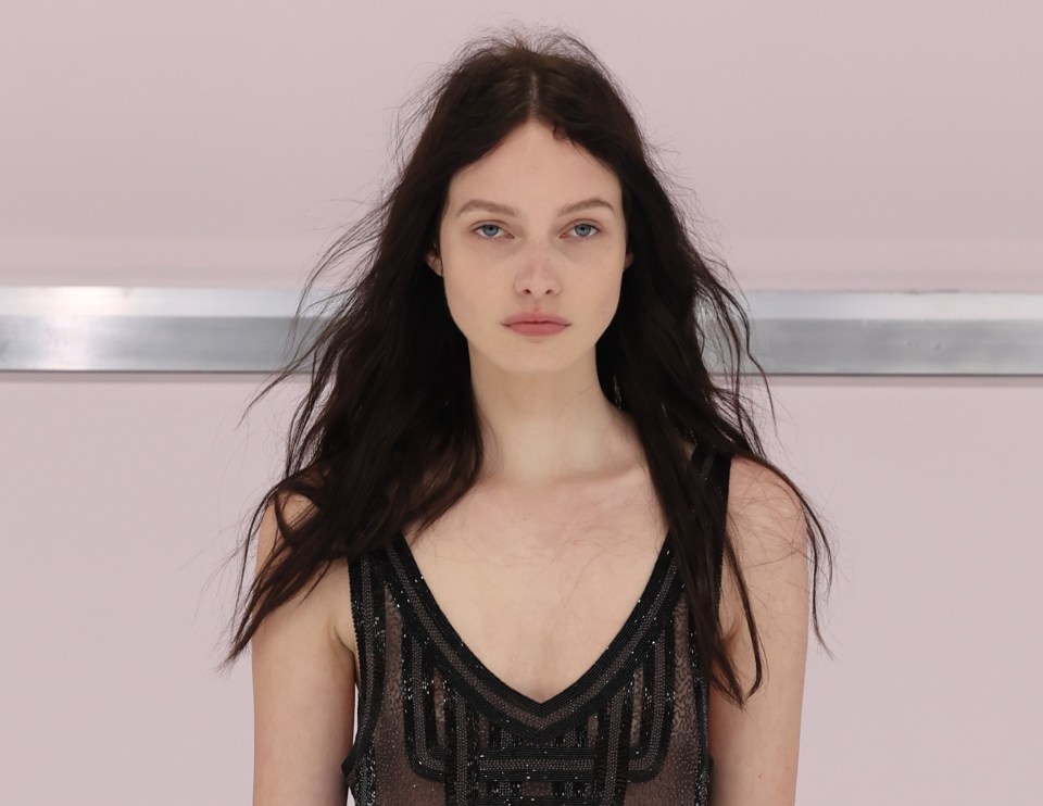 Model walking a Fendi runway in a fringed, sheer black dress.