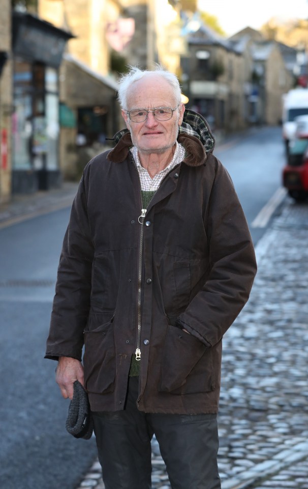 An older man stands on a cobblestone street in a village.