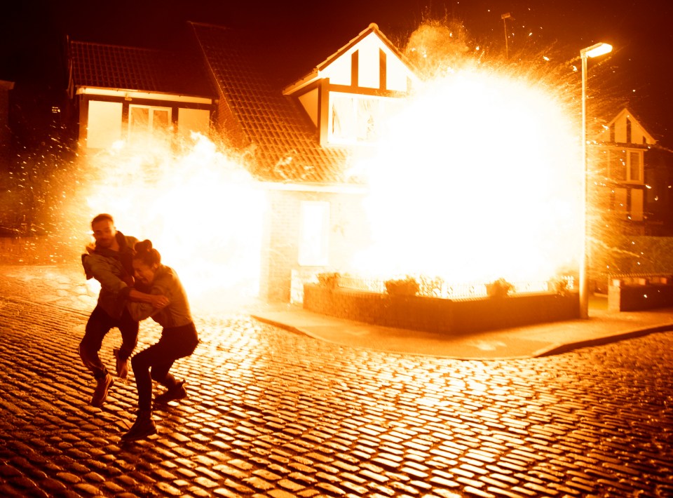 A house explodes as two people run away.