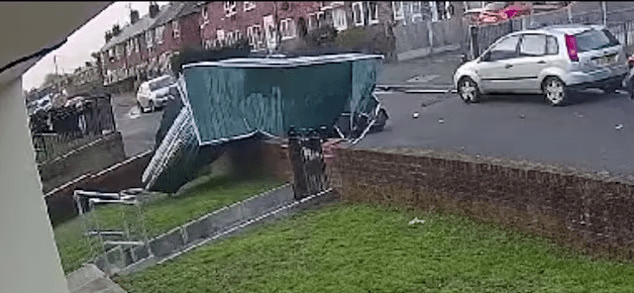A green dumpster tipped on its side after a collision with a car.