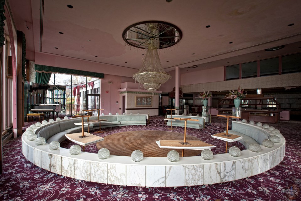 Interior of an abandoned honeymoon hotel with a circular seating area and a large chandelier.