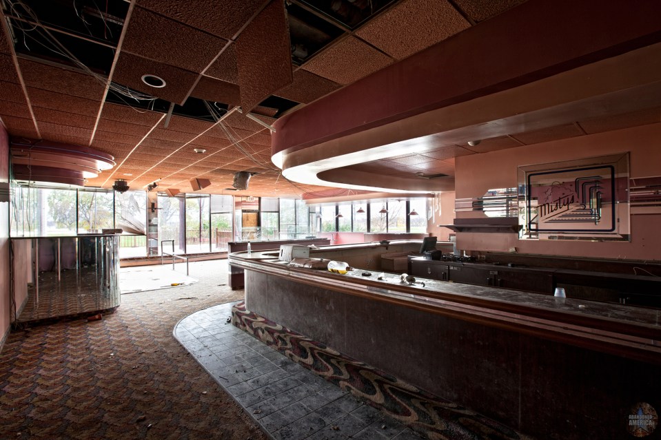 Interior of an abandoned bar with a damaged ceiling and dusty bar.
