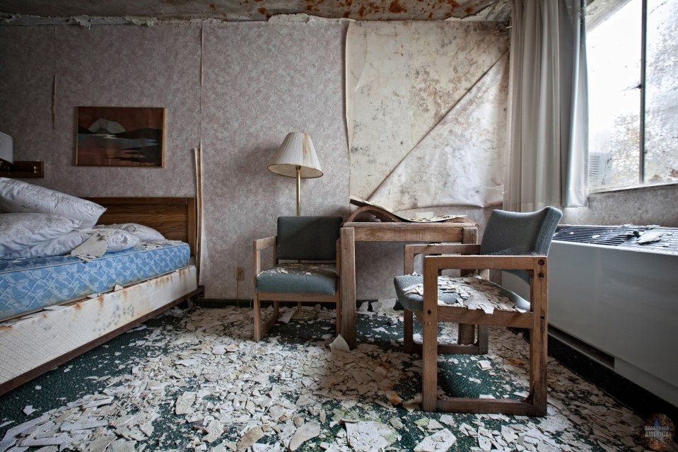 Decaying hotel room with damaged furniture and walls.