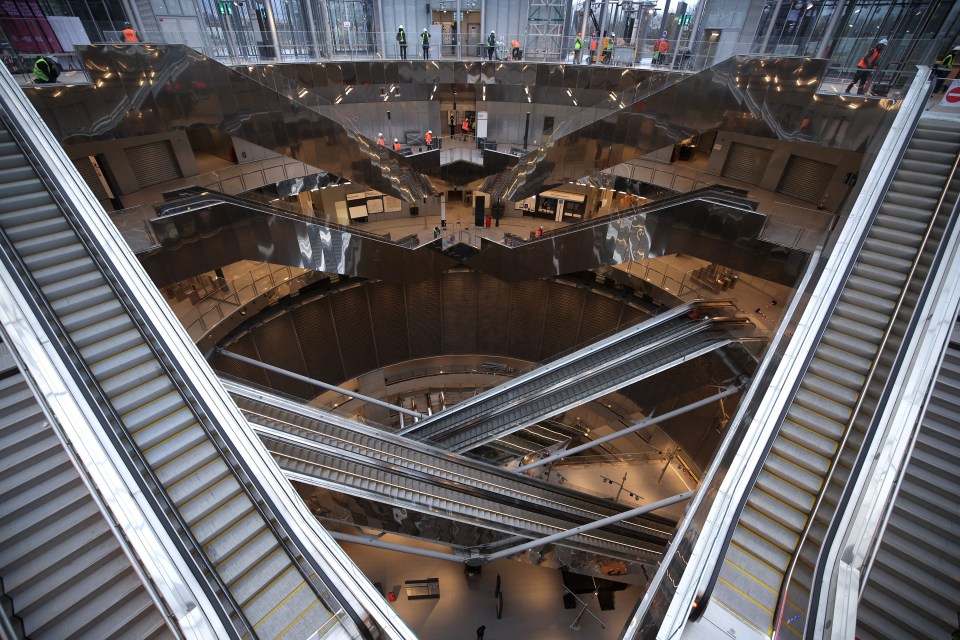 Interior view of a modern transportation hub under construction, featuring multiple escalators and workers.