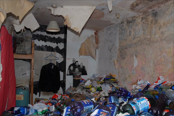 Messy room with damaged walls and floor covered in trash.