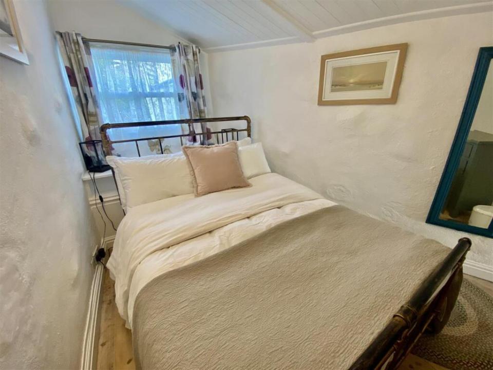 Interior of a narrow bedroom with a bed, a small window, and a mirror.
