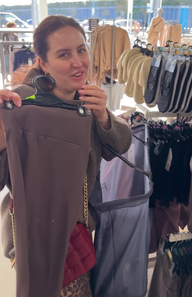 Woman holding up brown leggings in a clothing store.