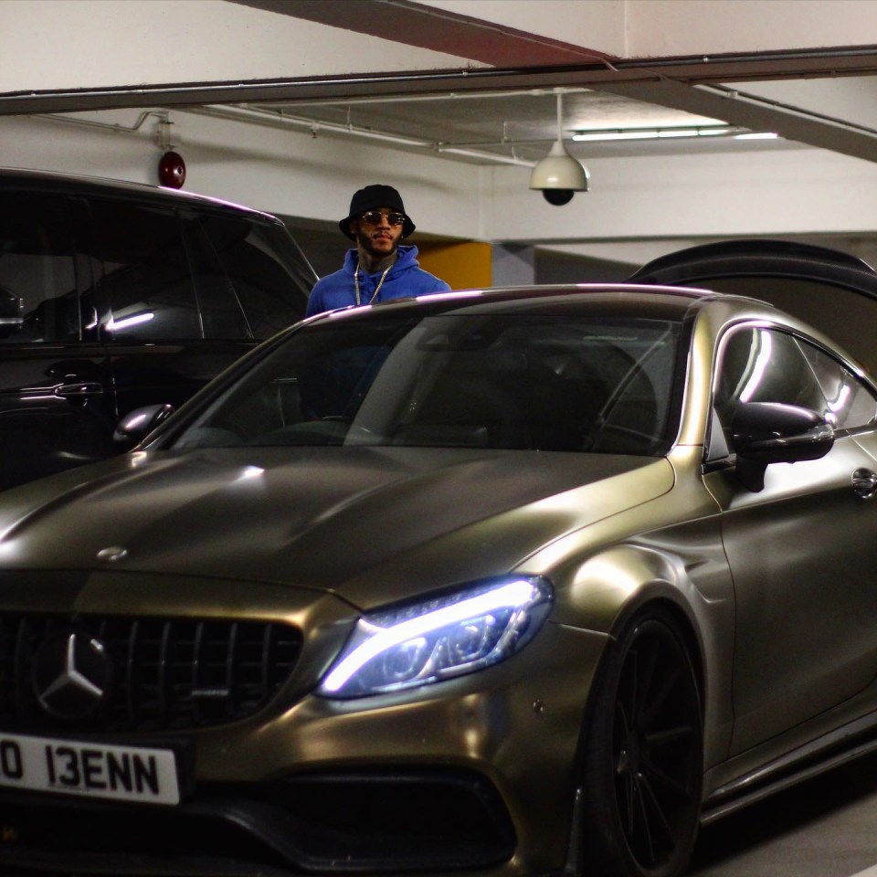 Man in blue hoodie standing by a dark-colored Mercedes-Benz.