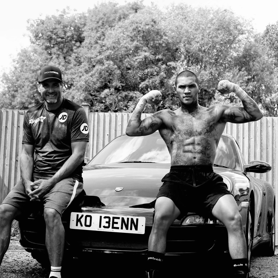 Black and white photo of a boxer and his trainer posing with a car.