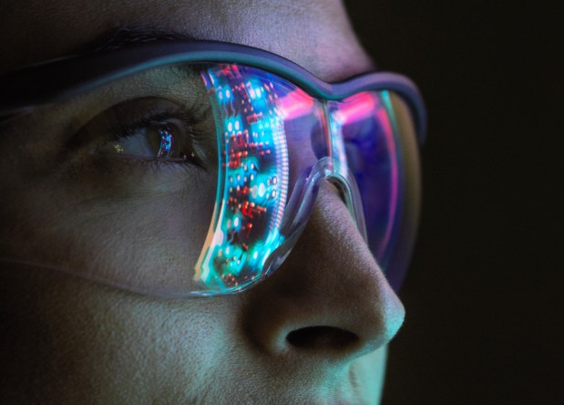 Close-up of a woman's eye and nose, with a circuit board reflected in her safety glasses.