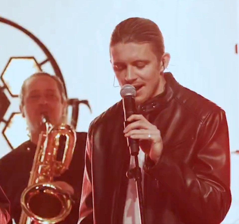 Singer holding a microphone, with a saxophonist in the background.