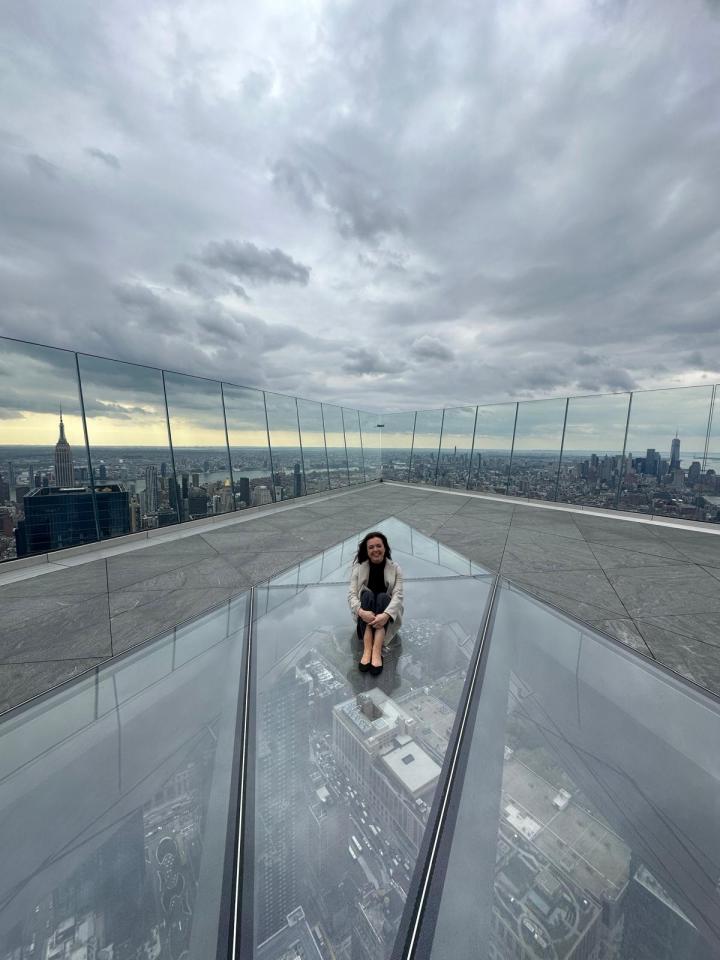 Woman sitting on a glass floor overlooking NYC.