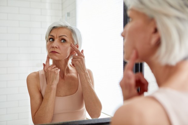 A mature woman examines her face in a mirror.