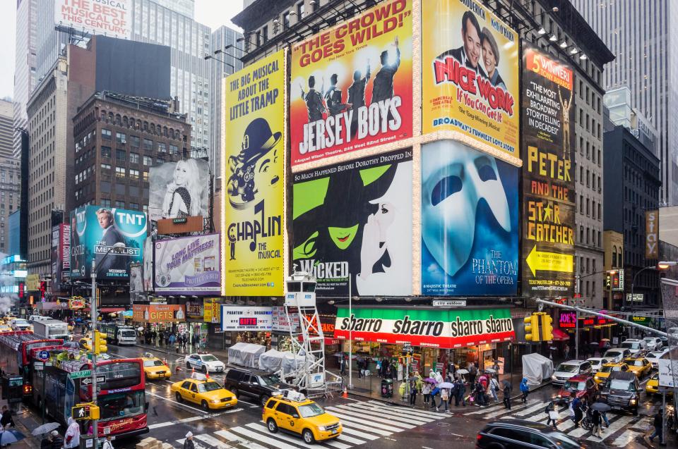 Broadway theater district in New York City with billboards and street traffic.