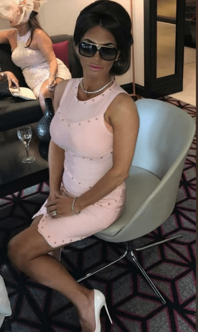 Woman in pink dress and sunglasses sitting in a chair.